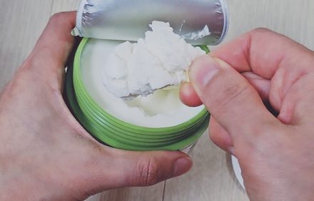 Scooping cleansing balm from a green jar