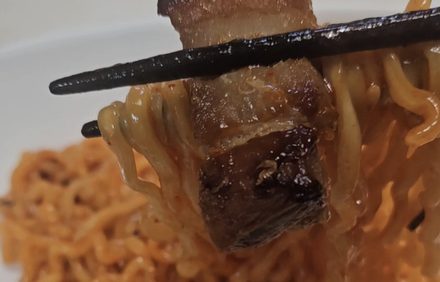 Pork belly lifted from a bowl of Korean instant noodles
