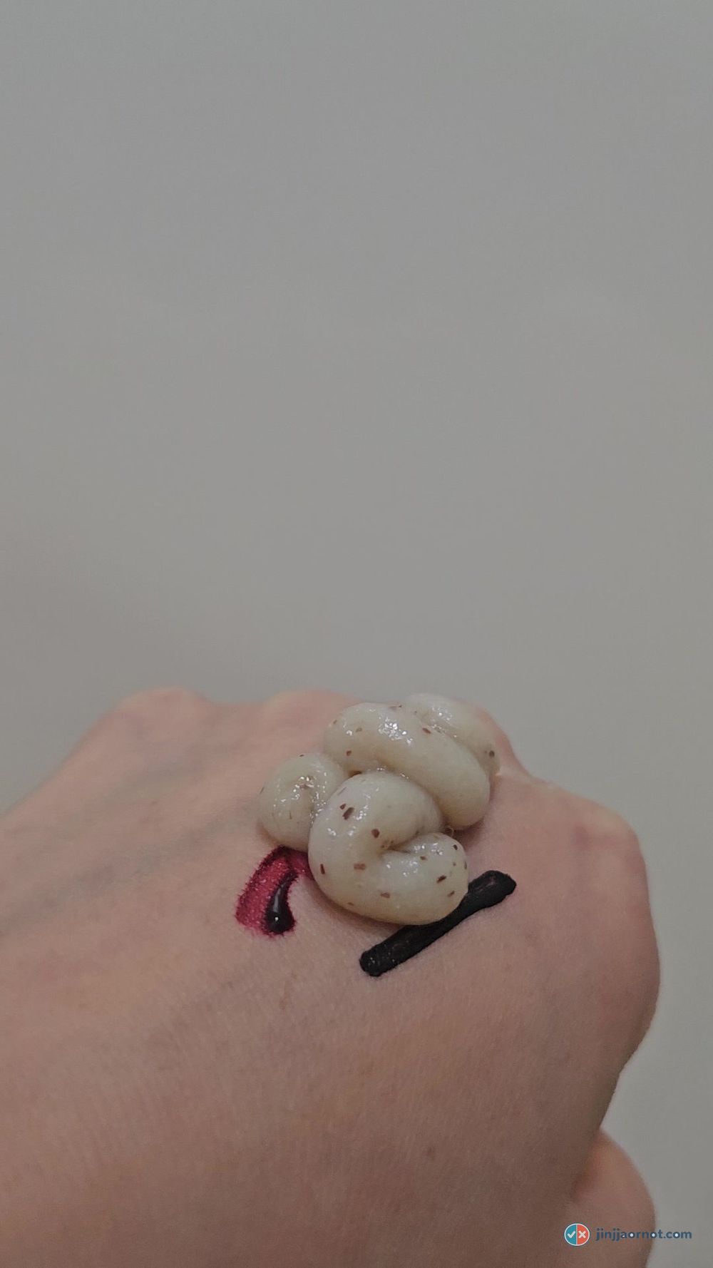 Anua cleansing foam on the back of a hand with visible brown scrub particles, beside a tint swatch and an eyeliner line