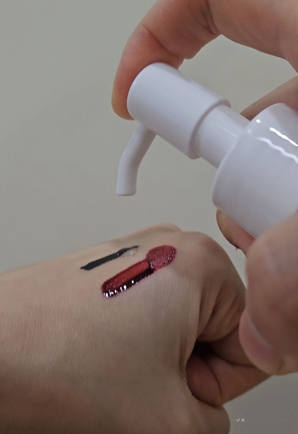 Black eyeliner and red lip tint swatched on the back of a hand next to the Anua pump
