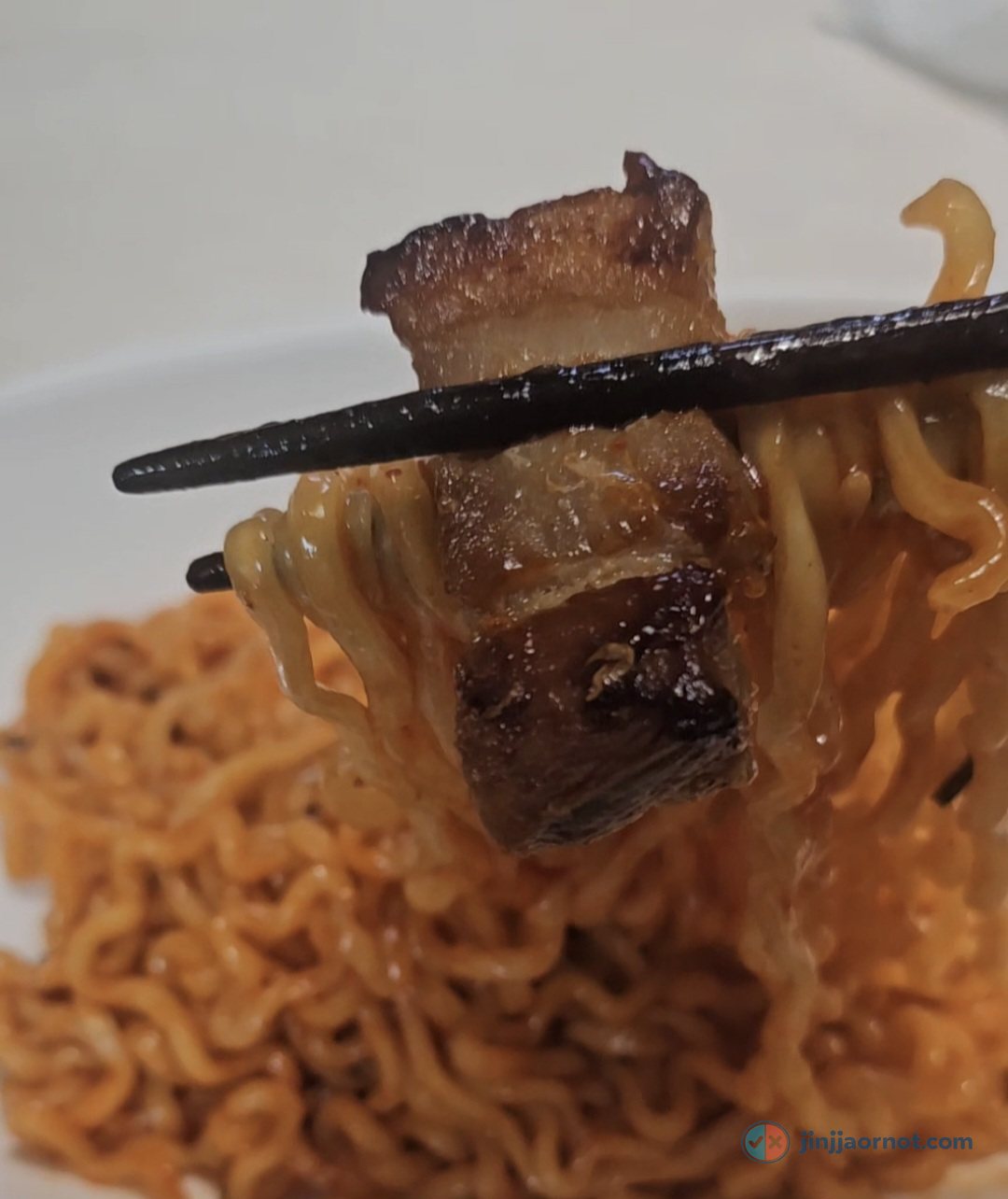 Chopsticks holding creamy Buldak Carbonara noodles topped with a piece of kimchi