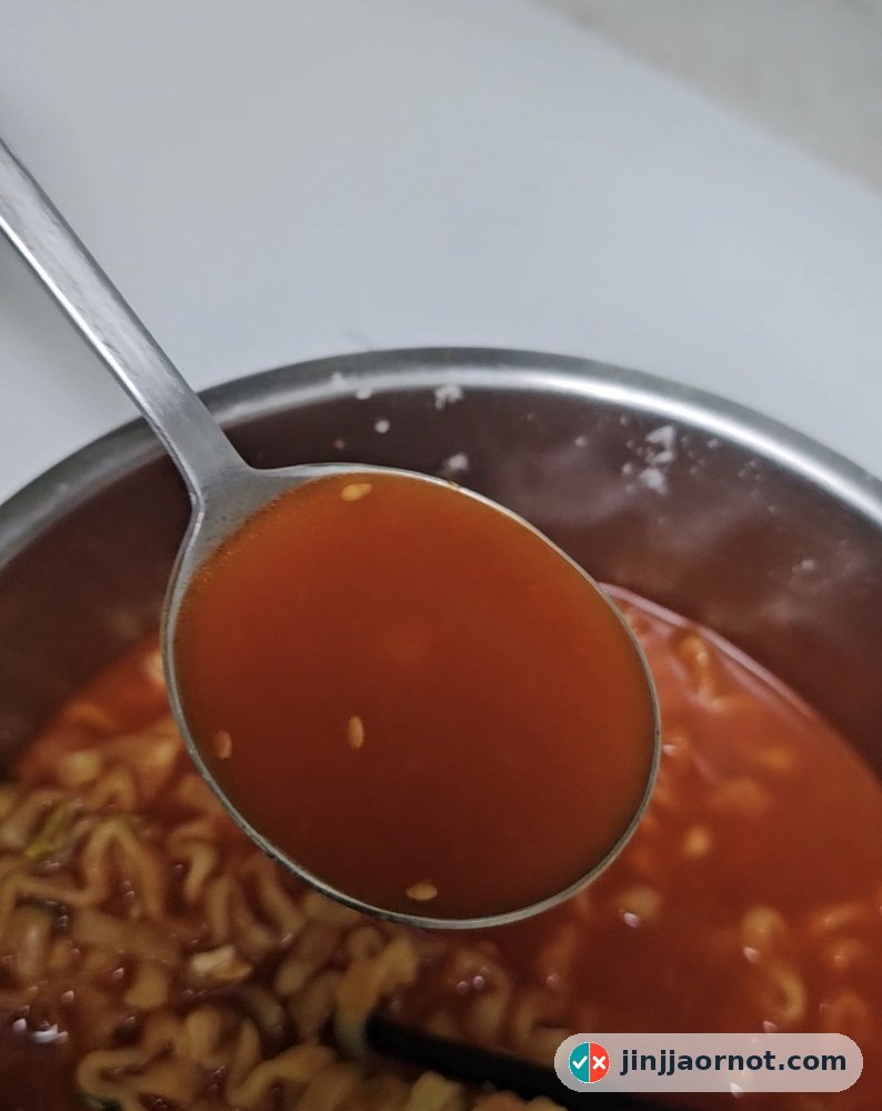 A spoonful of red Buldak Tang broth lifted from the pot