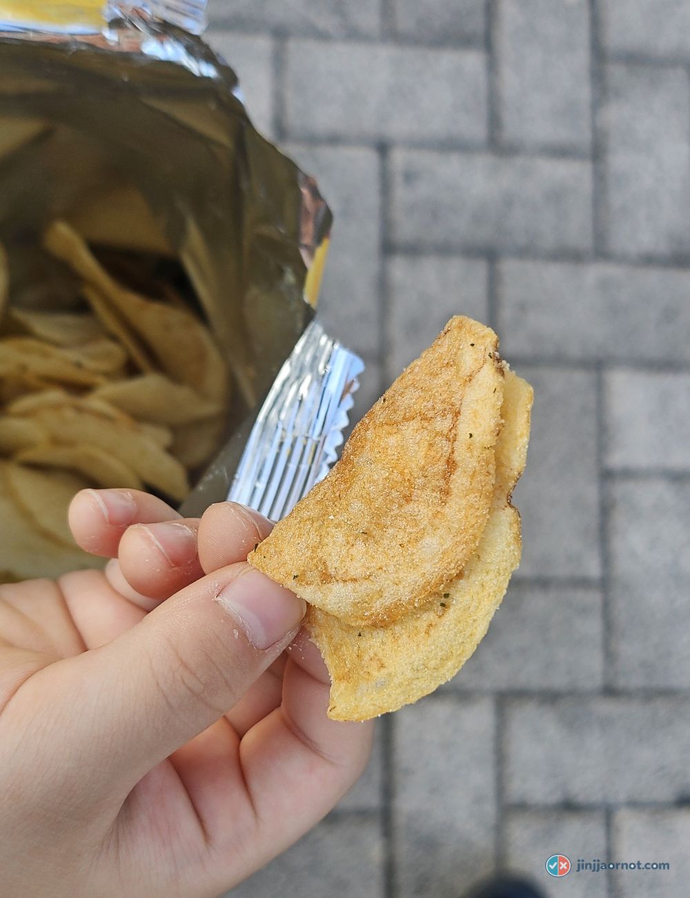 A single Honey Butter Chip held between two fingers showing the pale seasoning