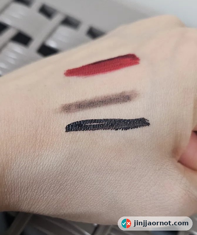 Three makeup swatches on the back of a hand: red lip tint, brown pencil, and black waterproof eyeliner