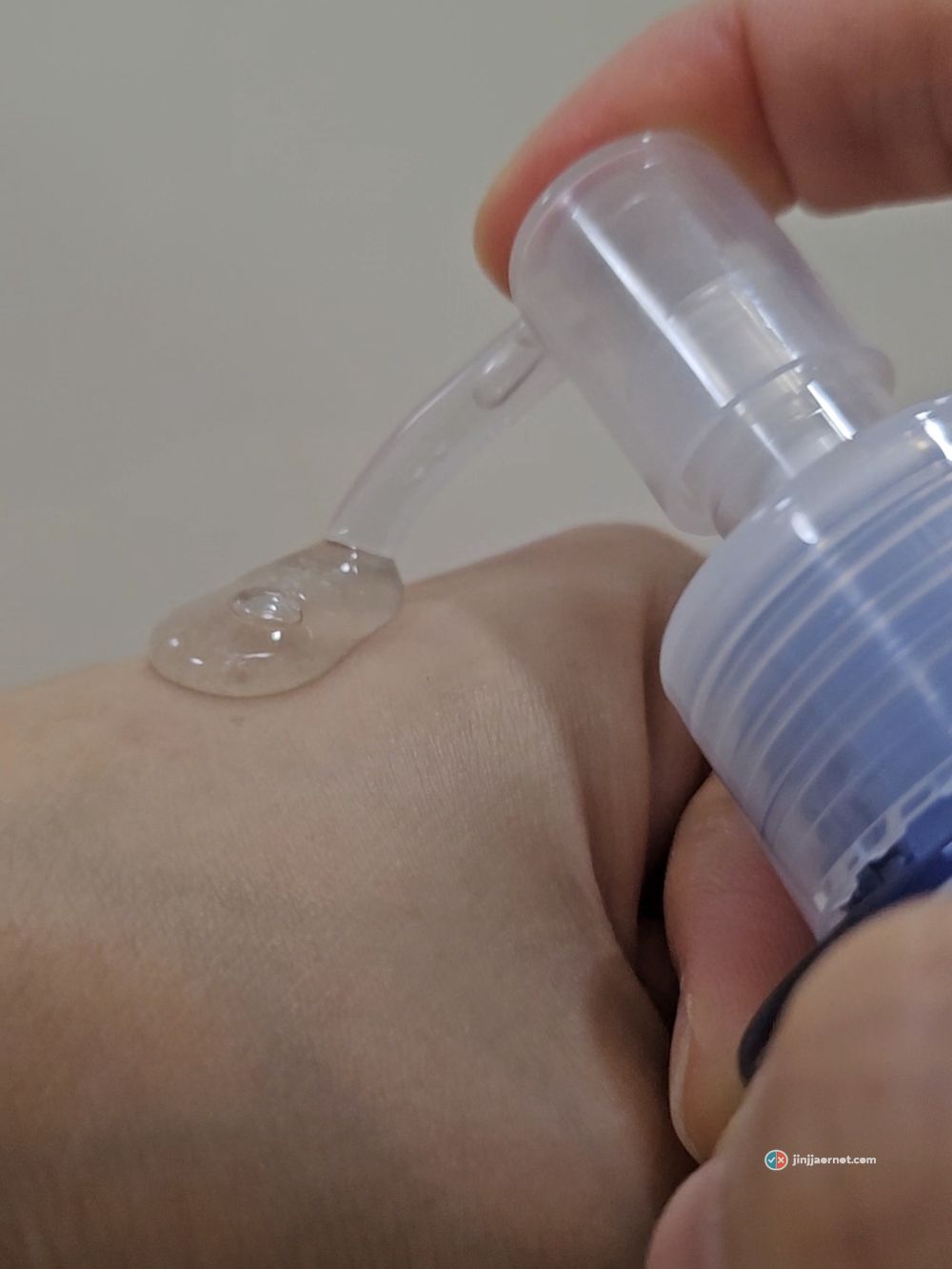 Clear gel cleanser dispensed from a blue pump bottle onto the back of a hand