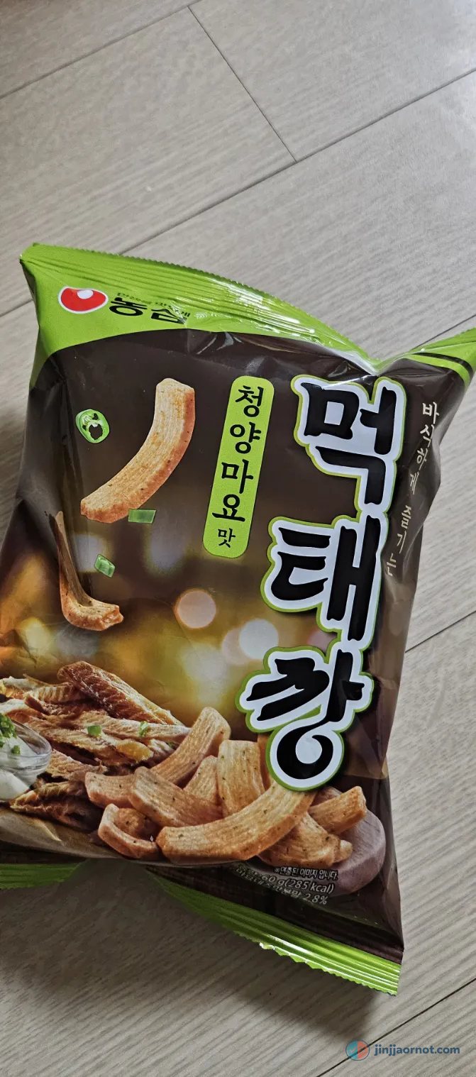 A bag of Nongshim Mektaekkang Cheongyang Mayo chips, green and brown packaging, held over a floor