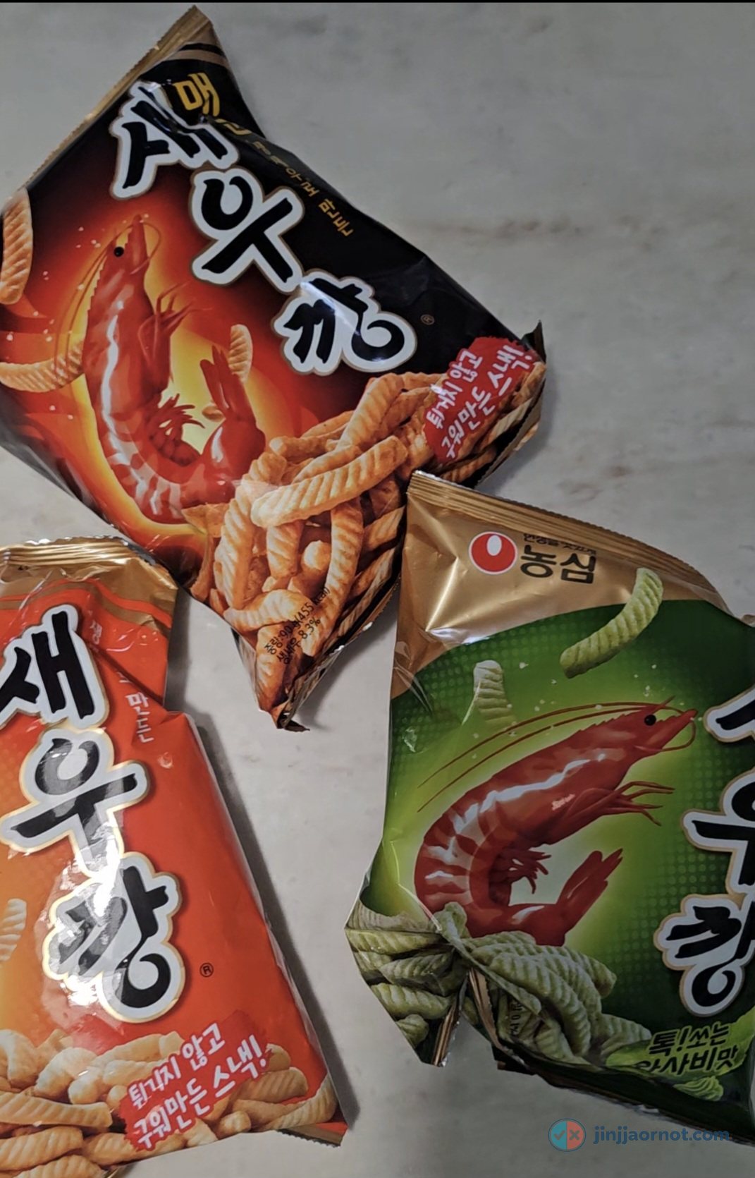 Three bags of Nongshim Saewookkang shrimp chips arranged on a counter: Spicy in black, Original in orange, and Wasabi in green
