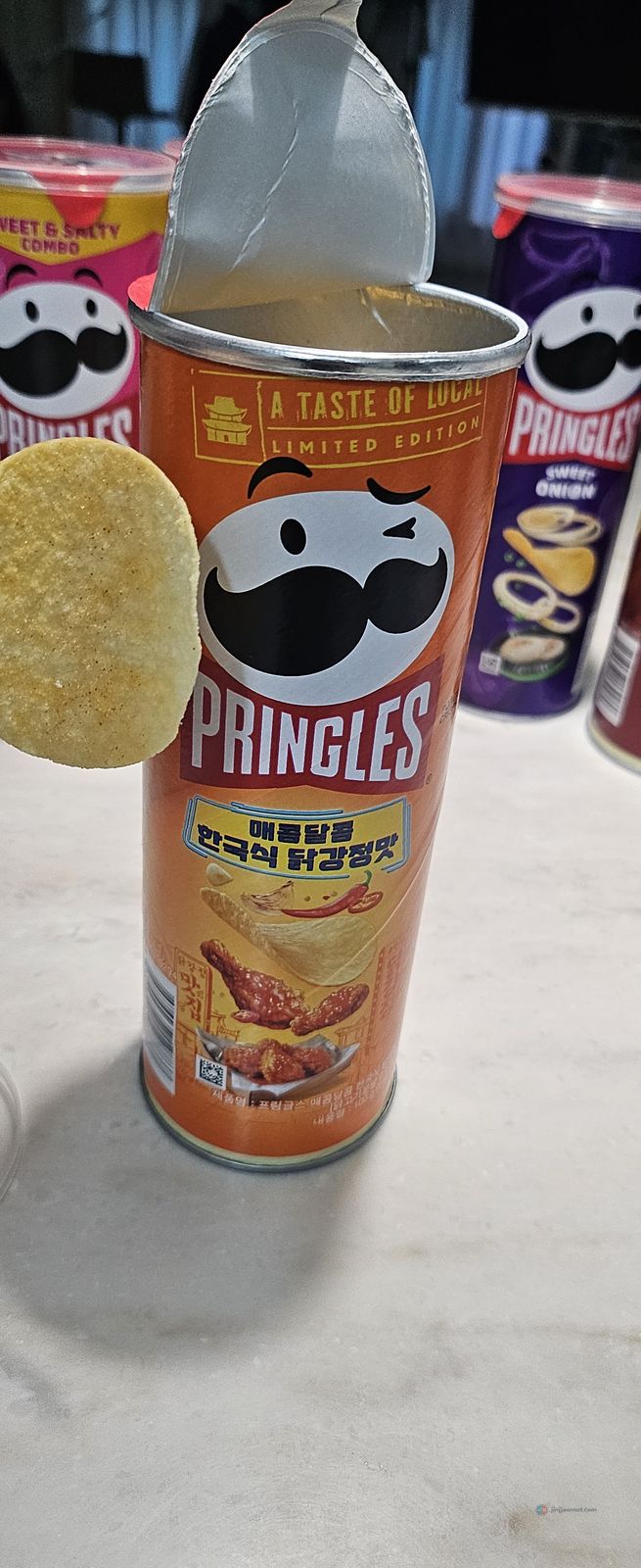 A single Korean Pringles crisp held up next to the open orange can of the Korean sweet and spicy chicken flavor